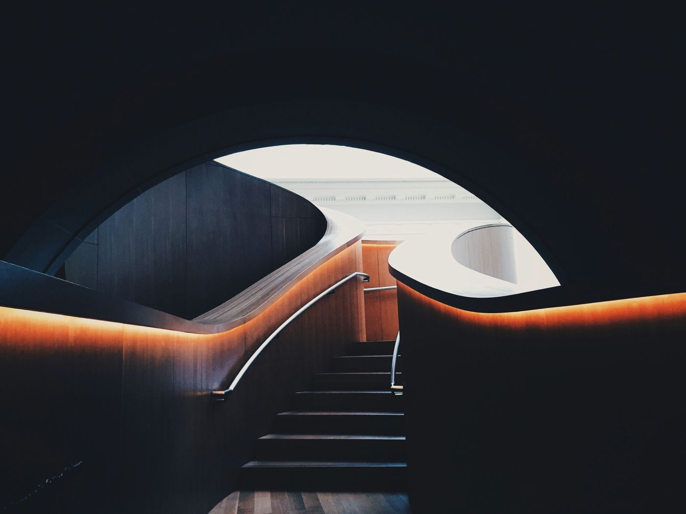Curved timber staircase lit by a concealed warm light strip